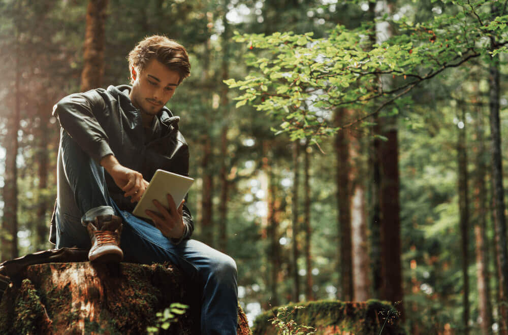 Main sitting on a rock in the woods with a tablet